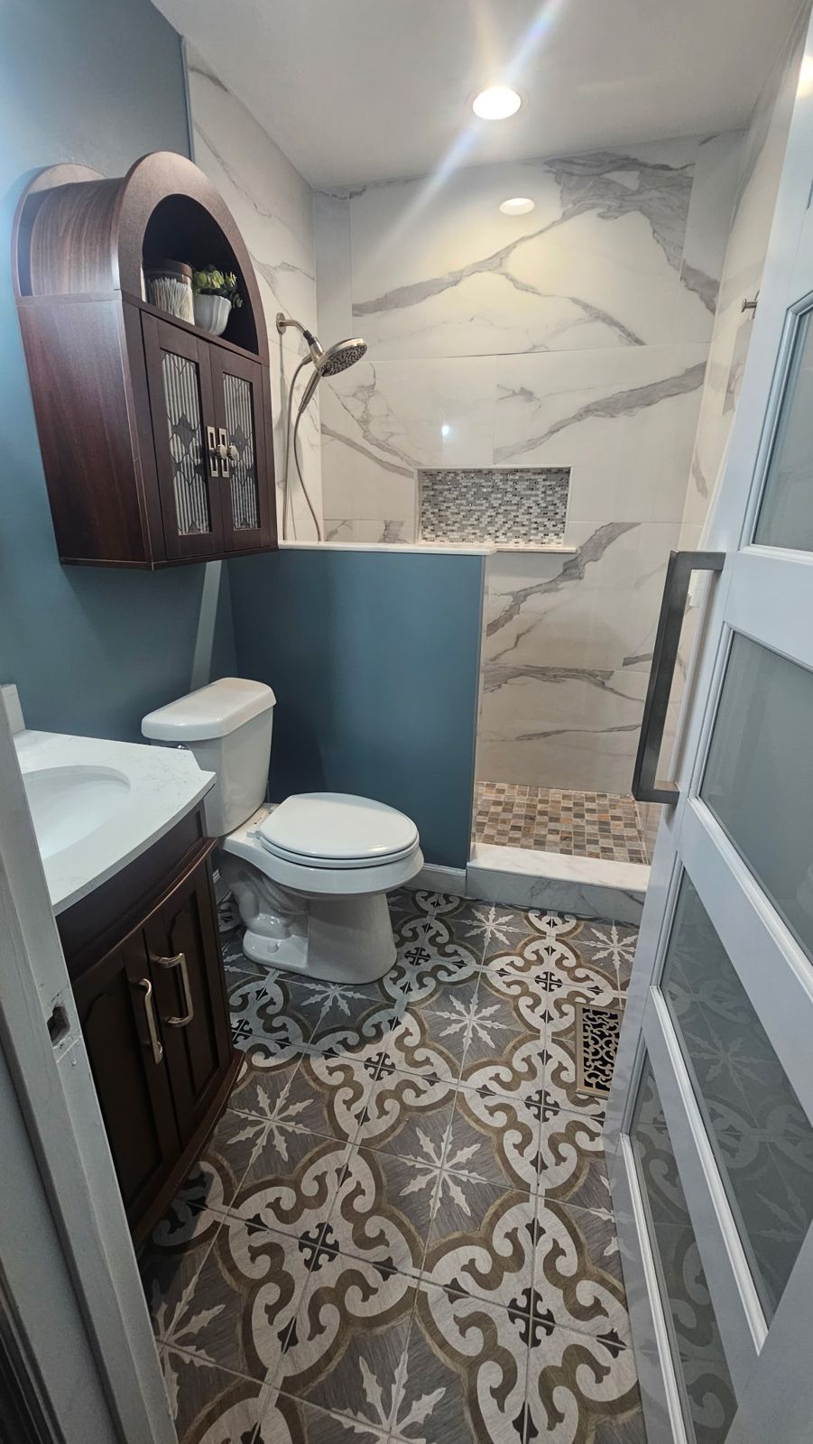 Finished bathroom remodel with marble-look tile shower, patterned floor tile and wood vanity