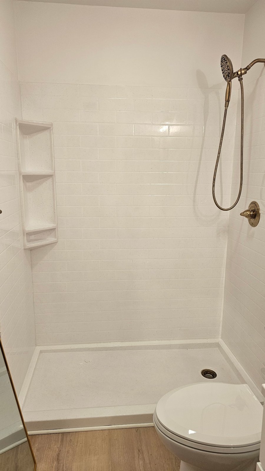 Close-up of a white Onyx Collection shower with subway-tile wall panels, corner shelf and brushed gold fixtures