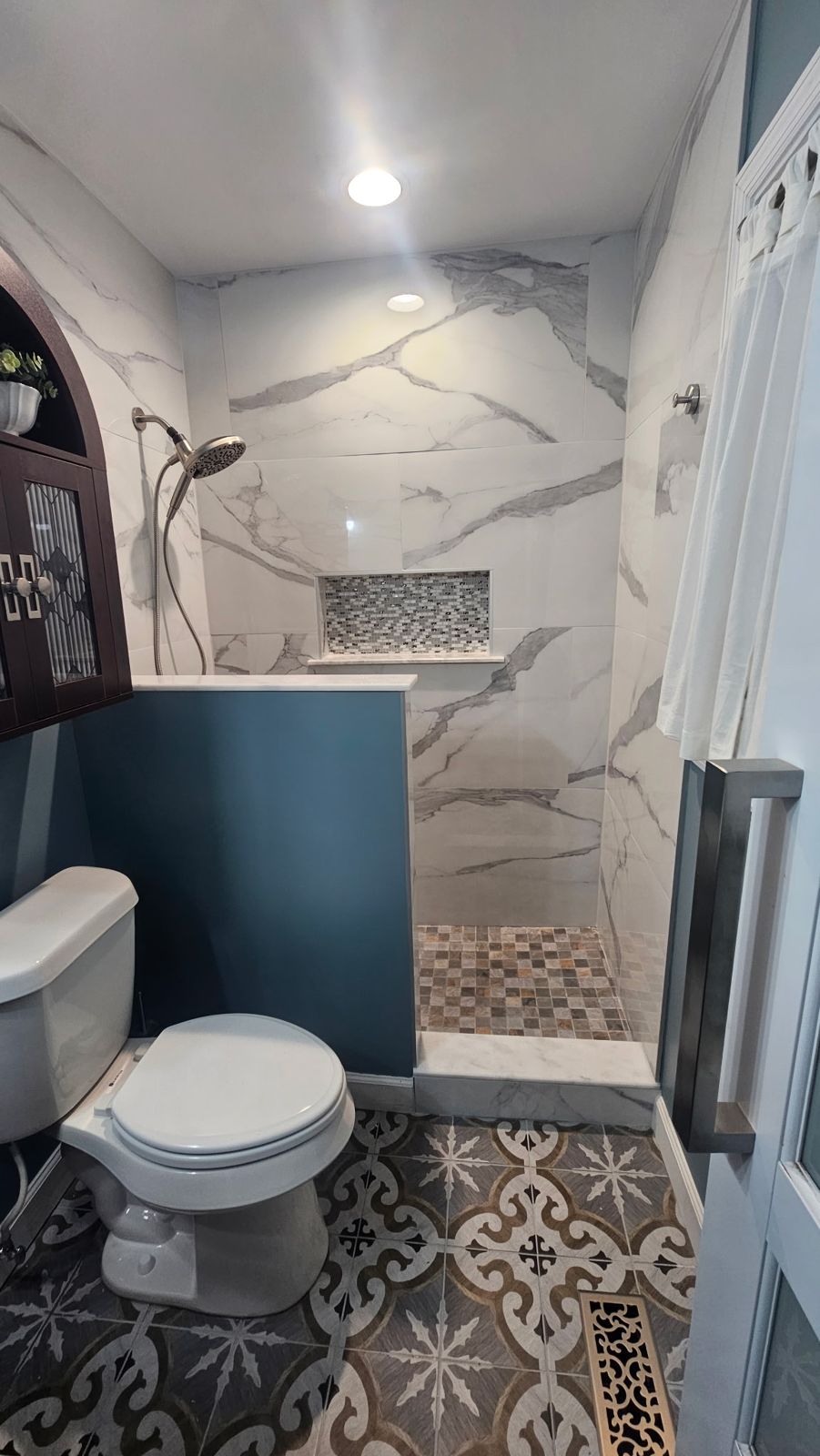 Marble-look tile walk-in shower with half wall above patterned floor tile